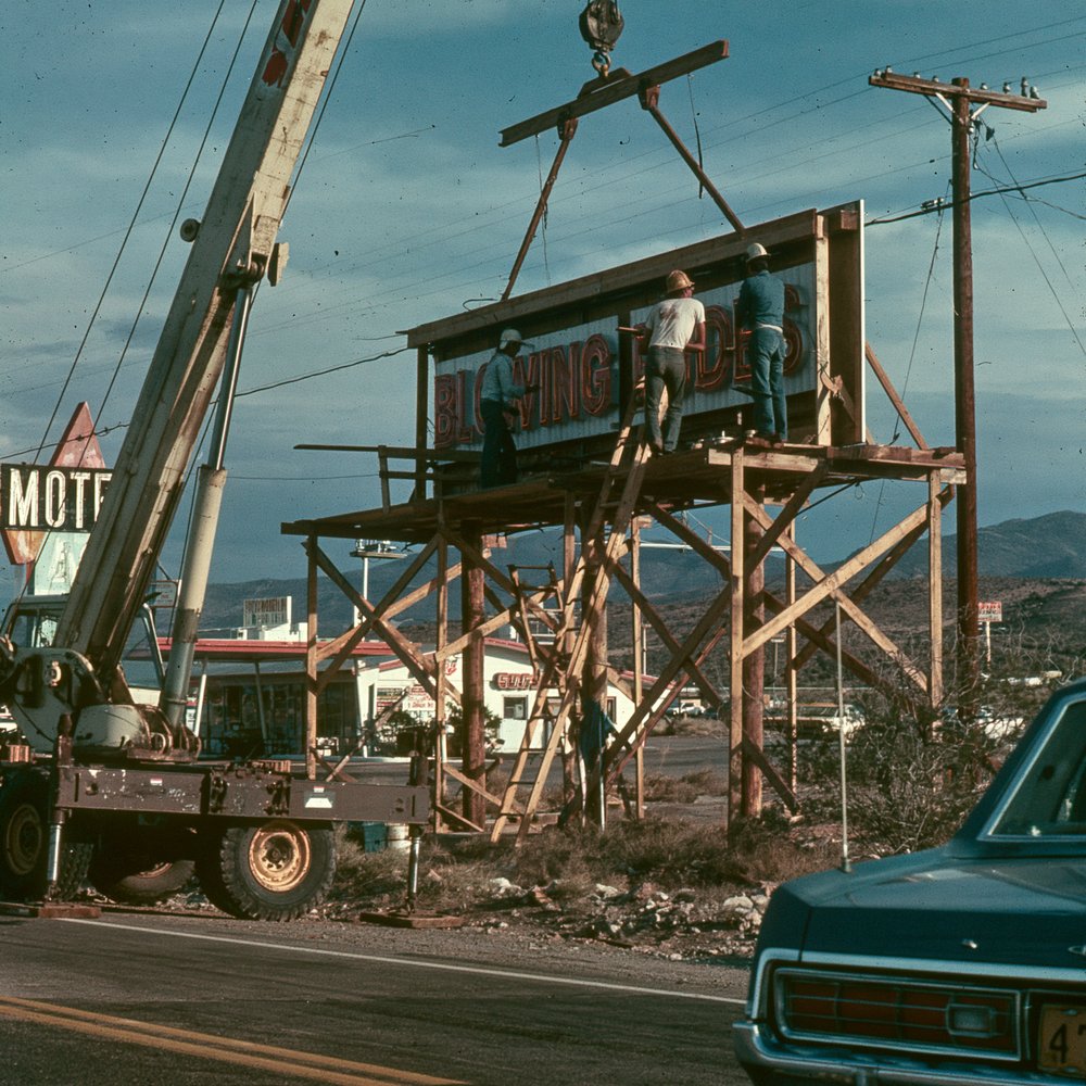 Workers installing the brand-new Blowing Dudes billboard on Route 66 in 1979, motel sign beside it